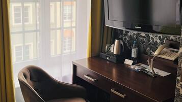 Ett hotellrum med en säng, ett skrivbord med en tv, en stol, en kaffebryggare och en telefon.