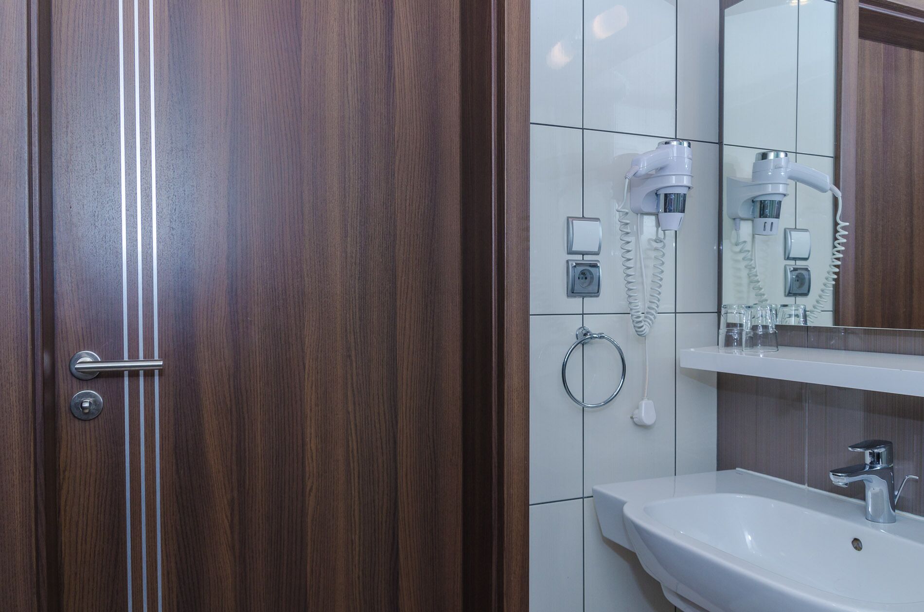 Une salle de bain avec une porte en bois, un lavabo blanc, un miroir et un porte-serviettes.