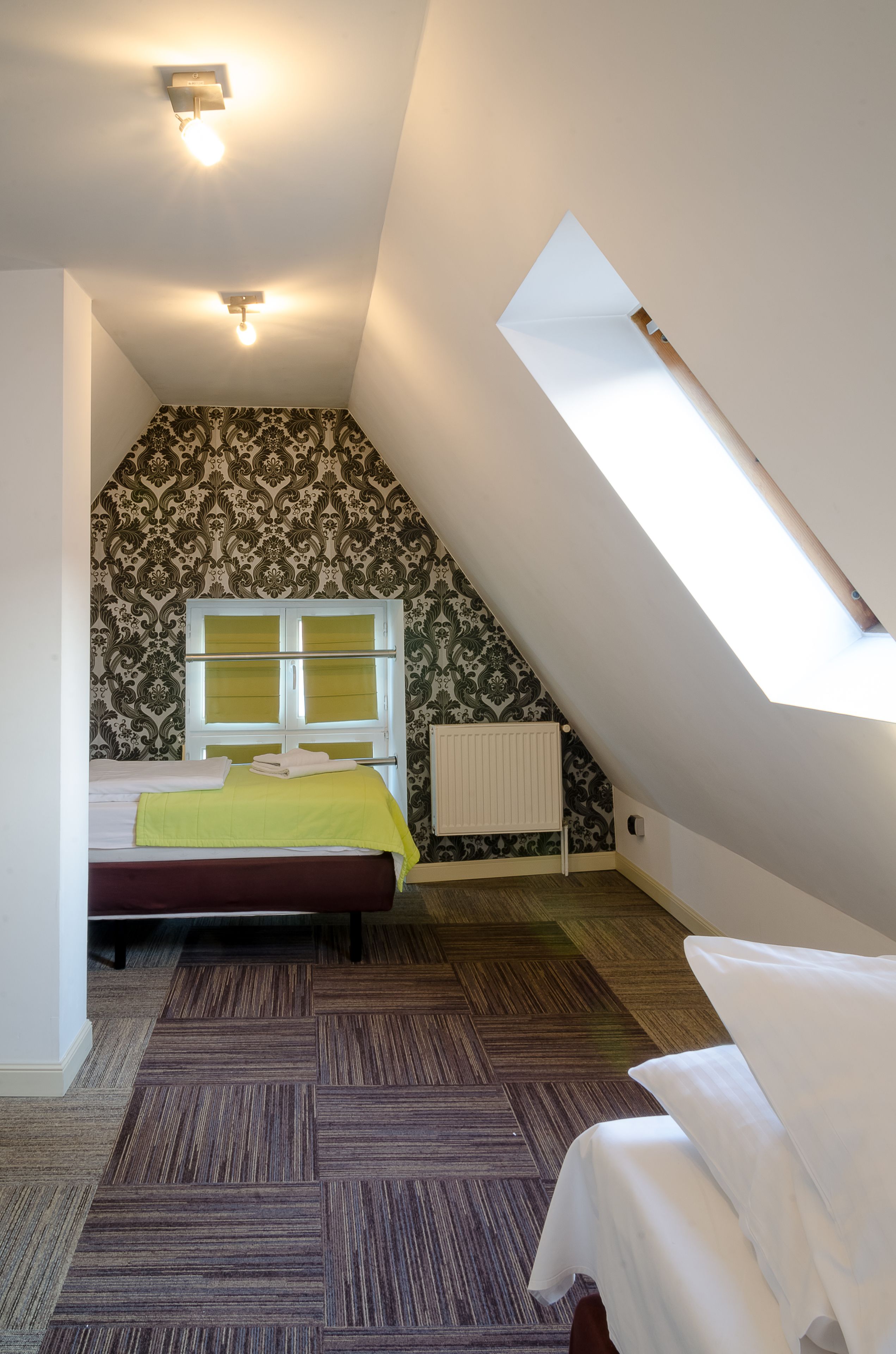 A small, triangular room with a bed, a radiator, and a skylight.