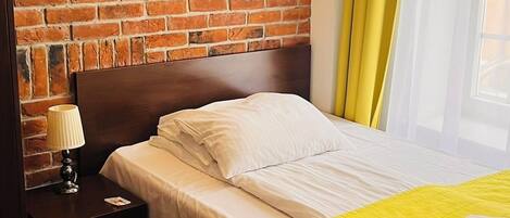 Ein Hotelzimmer mit Backsteinwand, einem hölzernen Kopfteil, einem Bett mit weißer Bettwäsche, einem Nachttisch mit Lampe und einer gelben Decke.