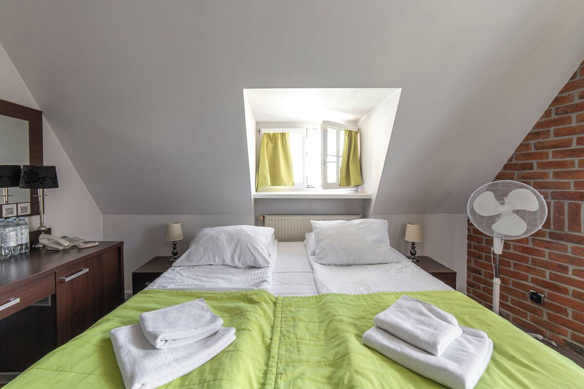 Hotellihuone, jossa on kaksi sänkyä, työpöytä, jossa on puhelin, lamput ja tuuletin.