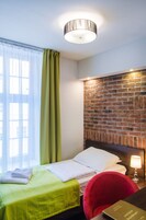 A hotel room with a bed, a red chair, a brick wall, and a window with curtains.