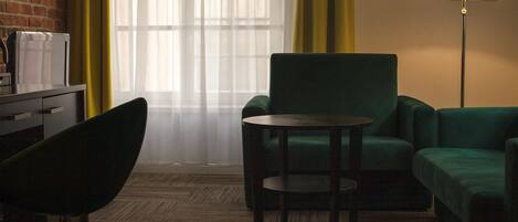 A room with a brick wall, a desk with a lamp, a green armchair, a round table, and a sofa.