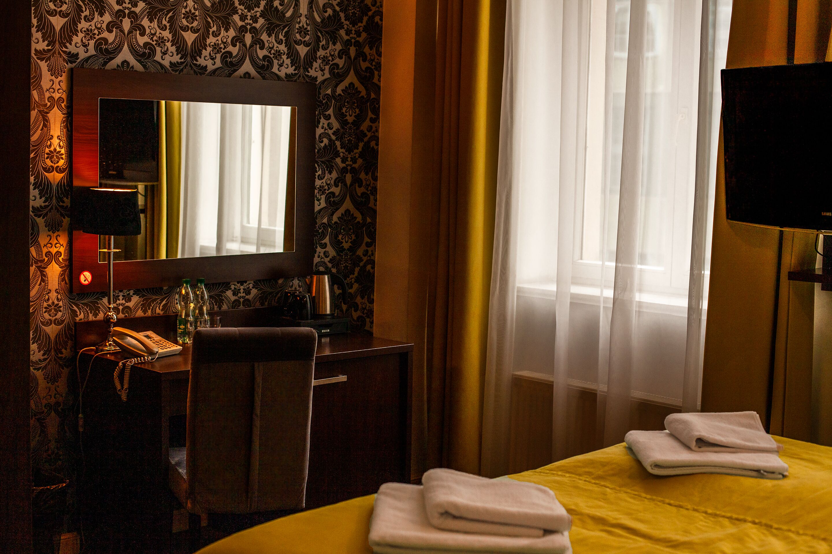 Una habitación de hotel con una cama, un escritorio con teléfono, una silla, un espejo y un televisor.