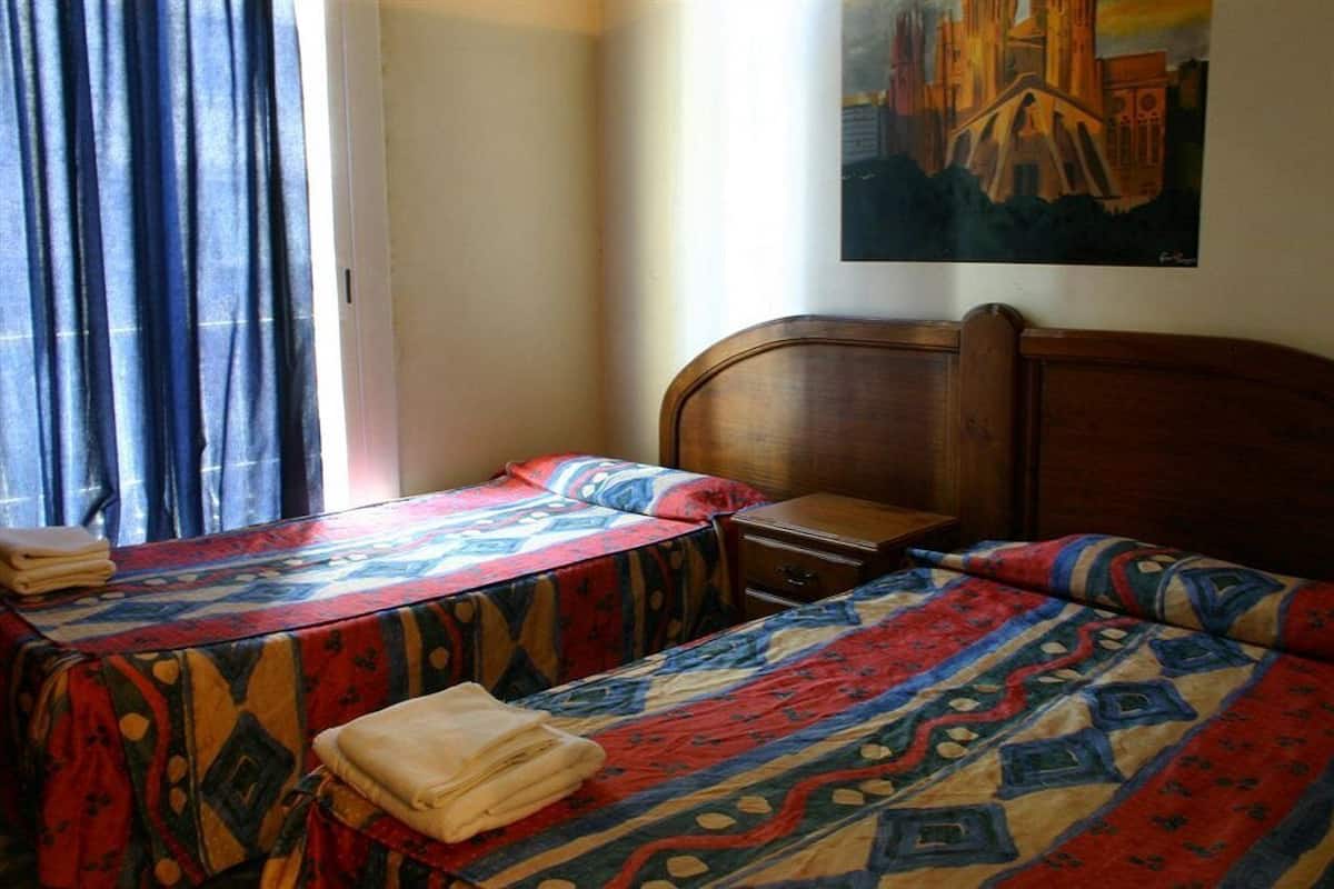 A hotel room with two beds, a wooden headboard, a nightstand, and a painting on the wall.
