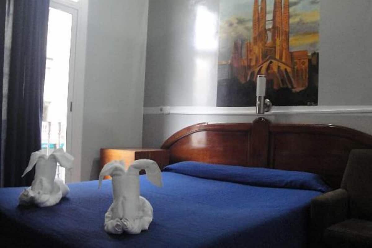 A hotel room with a bed, a chair, and a painting on the wall.
