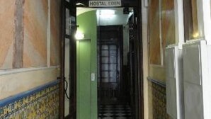 Un pasillo con piso a cuadros, una puerta verde con la leyenda 'HOSTAL EDEON' y un candelabro.