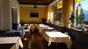 A dining area with tables set for four, a bench, and a window with a view of mountains. - Bellavista (Comelico Superiore)