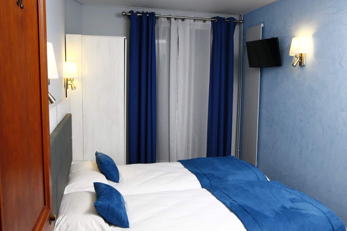 A bedroom with a bed, curtains, a television, and a wall-mounted light.