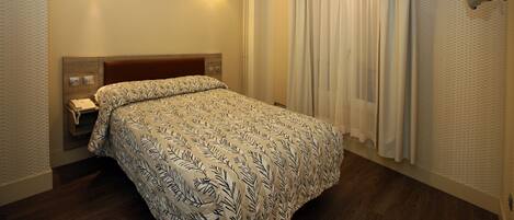 Una habitación de hotel con cama, teléfono junto a la cama y televisor montado en la pared.