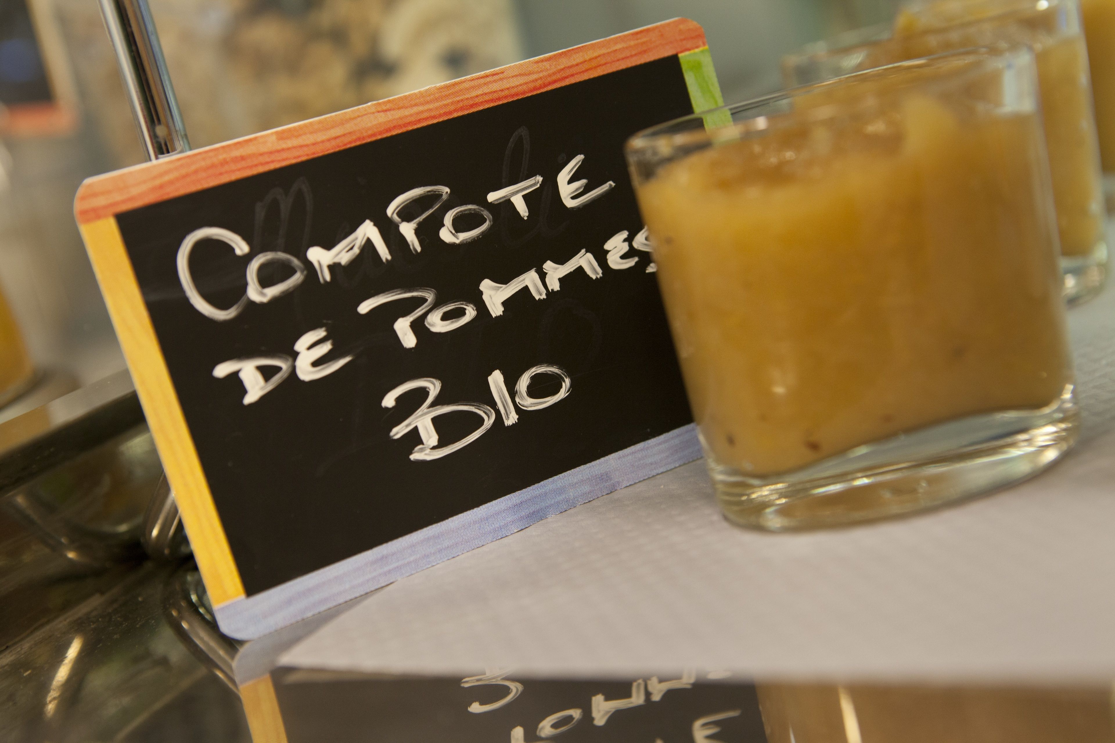 A chalkboard sign with handwritten text, a glass of a beverage, and a blurred background.