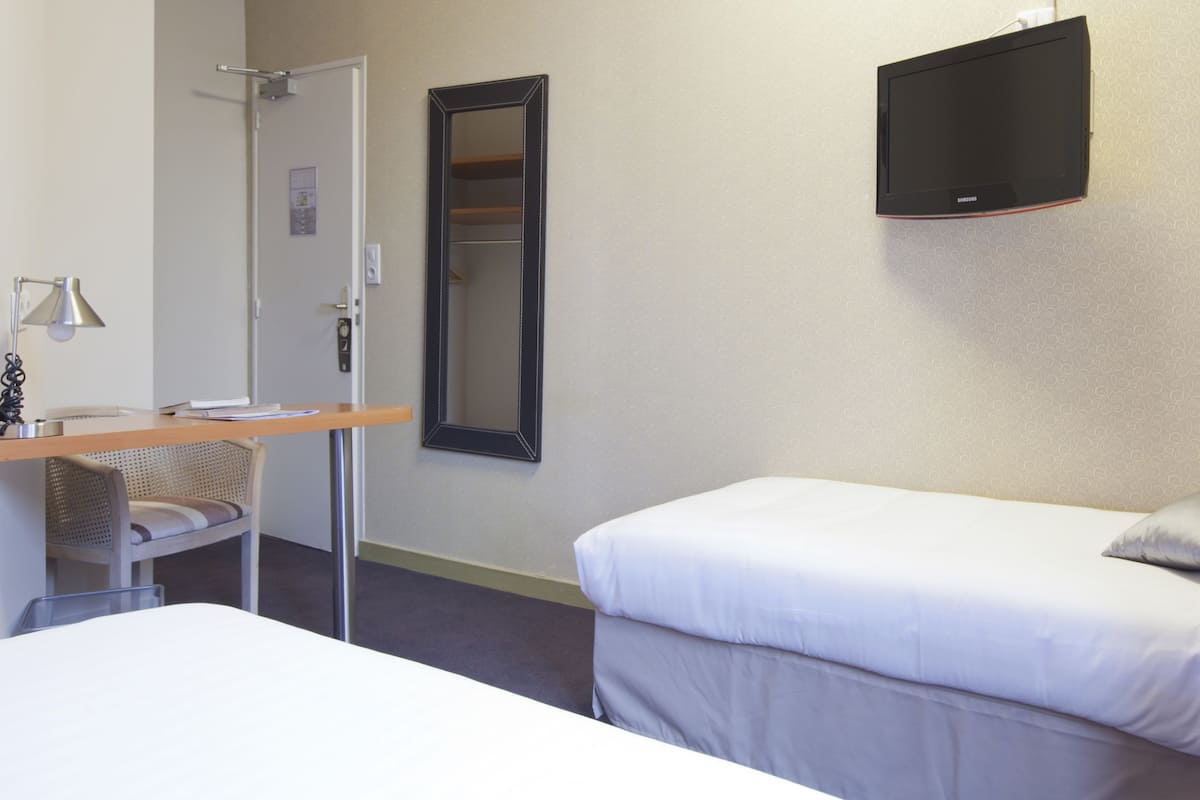 Habitación de hotel con una cama, un escritorio con una silla, un espejo y un televisor en la pared.