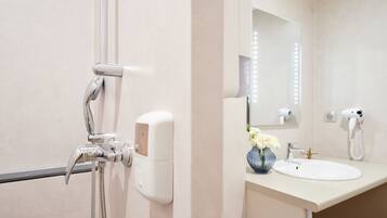 A modern bathroom with a shower, a hand dryer, and a vase with flowers on the sink.