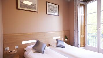 Une chambre d’hôtel avec deux lits, une tête de lit en bois, une table de chevet avec une plante et deux tableaux encadrés au mur.