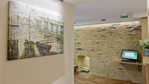 Zona de recepción con pared de piedra, un cuadro de barcos, un monitor de computadora y una pequeña mesa con teclado.