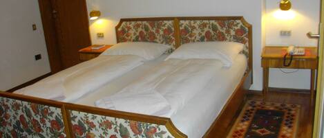 A double bed with floral headboard and footboard, a bedside table with a lamp, and a patterned rug on the floor.