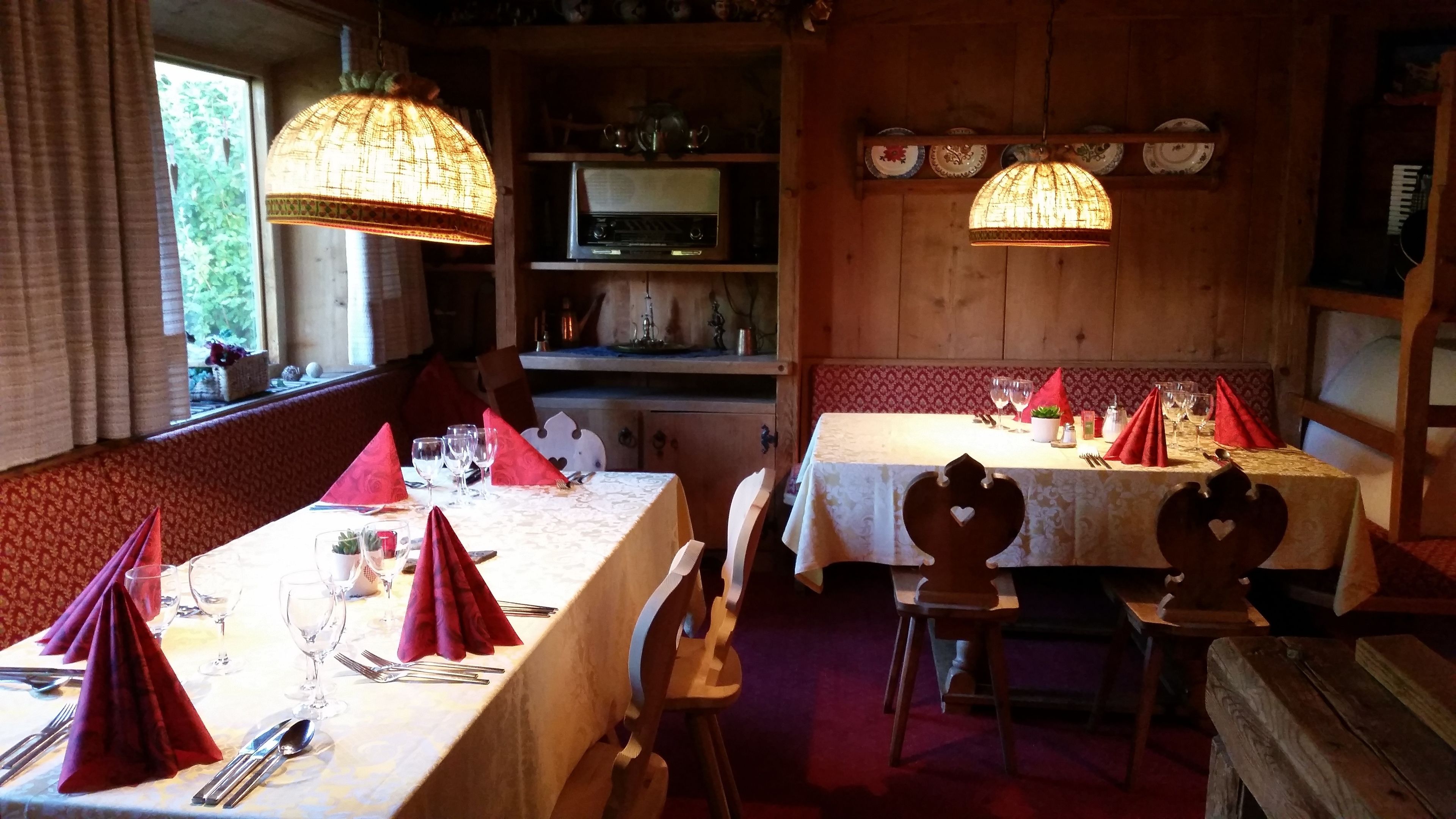 Un comedor con mesas de madera, servilletas rojas y lámparas colgantes.