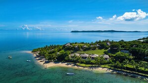 An aerial view of a coastal resort with beachfront villas, clear turquoise waters, and a small boat docked near the shore. - Volivoli Beach (Rakiraki)