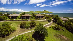 A resort with multiple bungalow-style buildings, a well-maintained lawn, and a view of the ocean and hills in the background. - Volivoli Beach (Rakiraki)