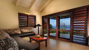 A modern living room with a sofa, a coffee table with a flower arrangement, and a view of the sea through large wooden doors. - Volivoli Beach (Rakiraki)