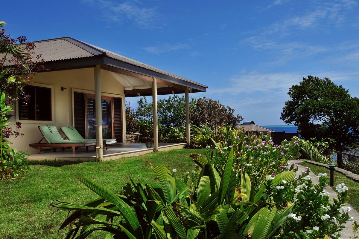 A house with a covered porch, a lawn, and a view of the sea.