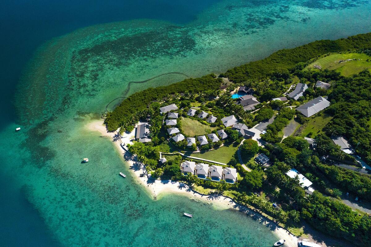 An aerial view of a coastal resort with multiple bungalow-style houses, a central pool, and a beach area.