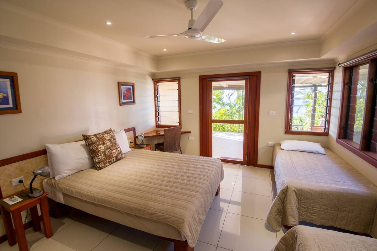 A hotel room with a large bed, a smaller bed, a desk, a chair, and a ceiling fan.