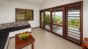 A room with a sofa, a small table with a plant, and a view of the sea through large glass doors.
