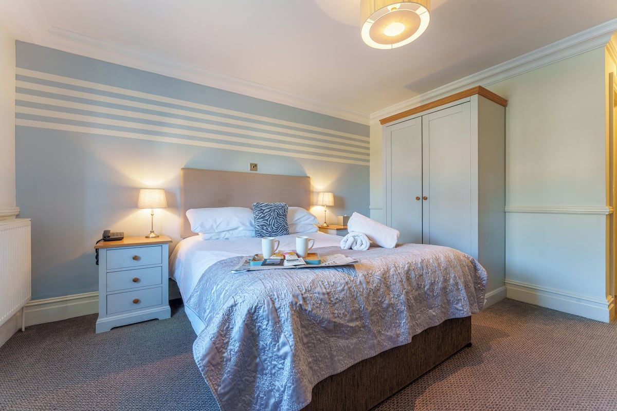A neatly made bed with pillows and a blanket, a bedside table with a lamp, and a wardrobe in a hotel room.
