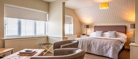 A bedroom with a large bed, a desk with a chair, and a window with blinds.