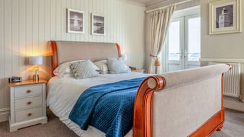 Una cama bien hecha con un edredón azul, una mesita de noche de madera con una lámpara y una ventana con cortinas.
