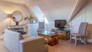 Un dormitorio estilo loft moderno con techo inclinado, un ventanal grande, un televisor de pantalla plana, una mesa de centro de vidrio, un sofá, una silla y un aparador.