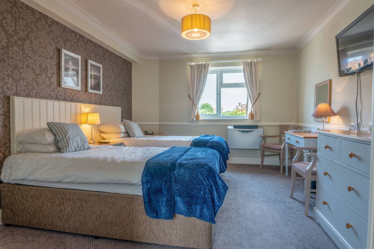 A bedroom with a bed, bedside lamps, a desk, and a dresser.