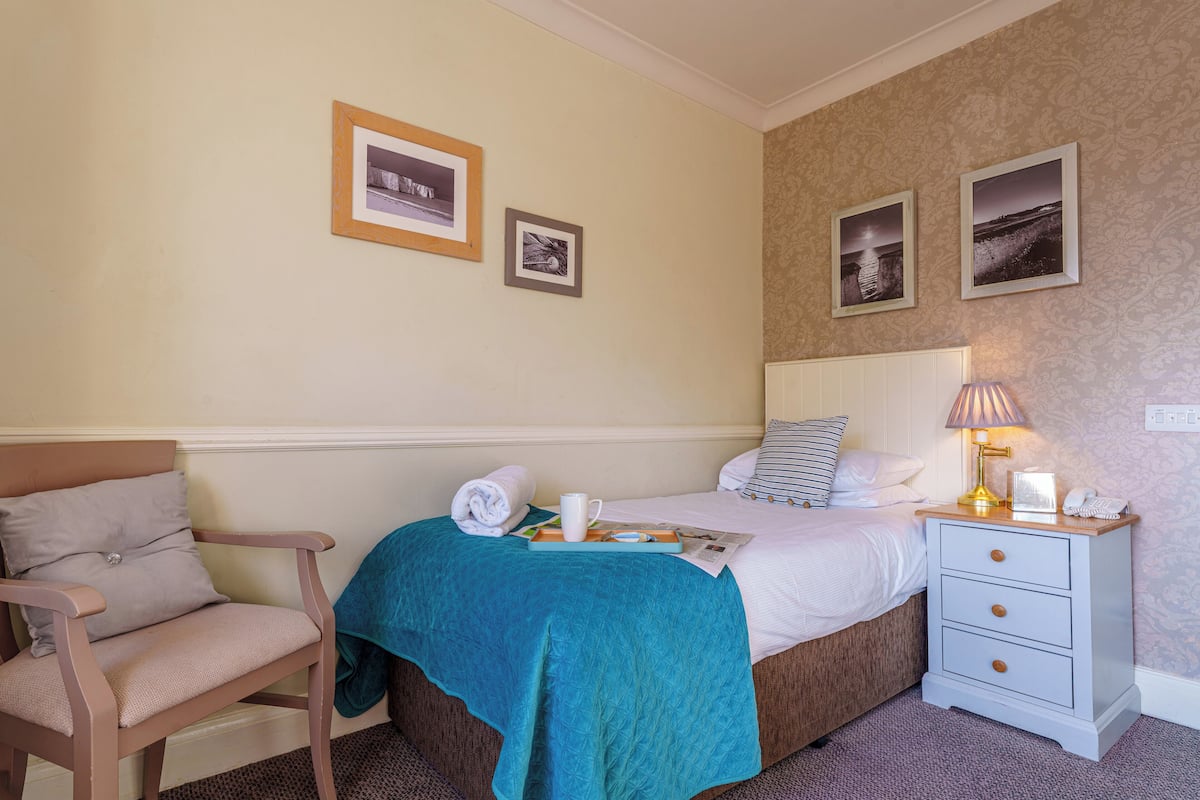 A neatly arranged bedroom with a bed, bedside table, chair, and wall-mounted pictures.