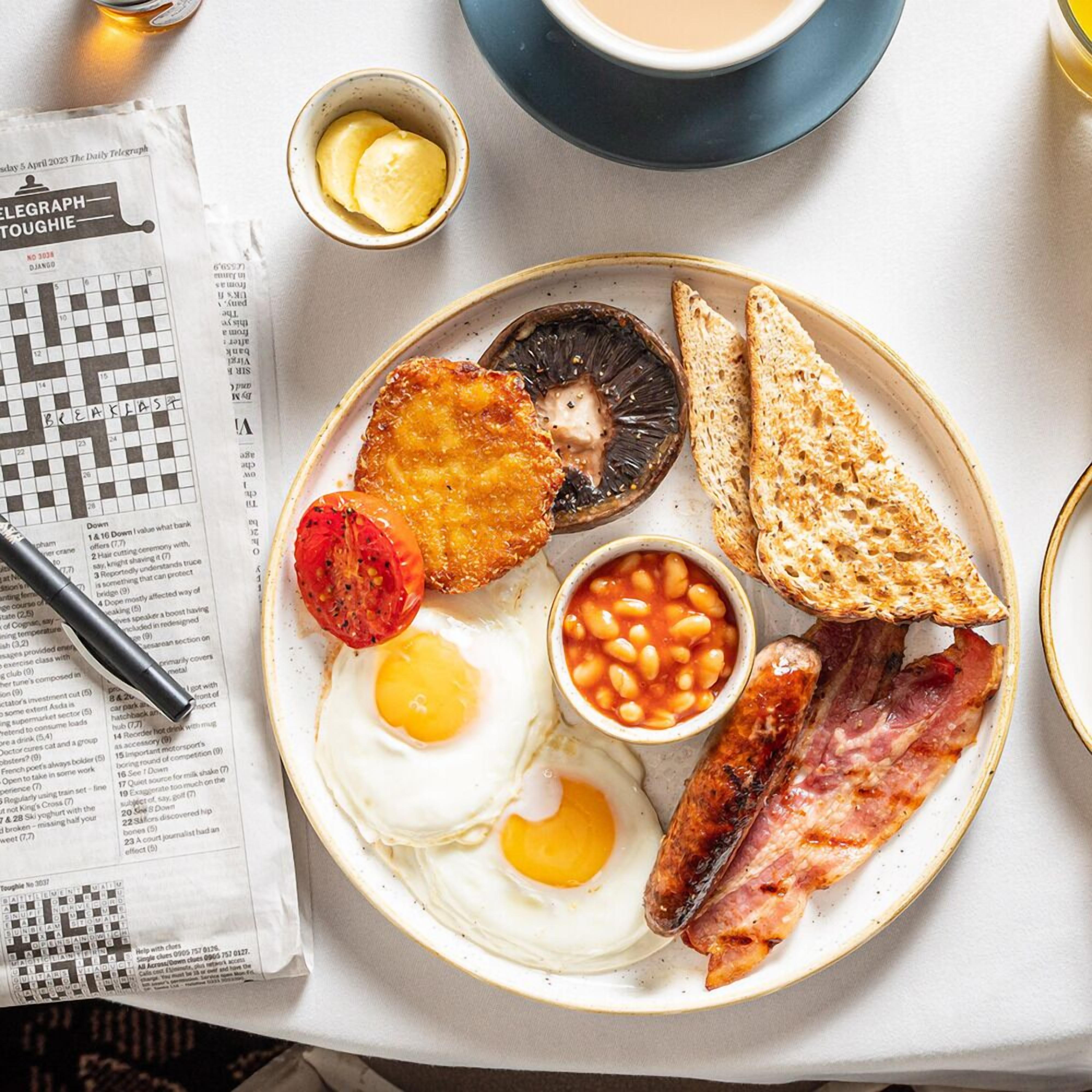 A breakfast plate with eggs, bacon, beans, toast, and a fried tomato.
