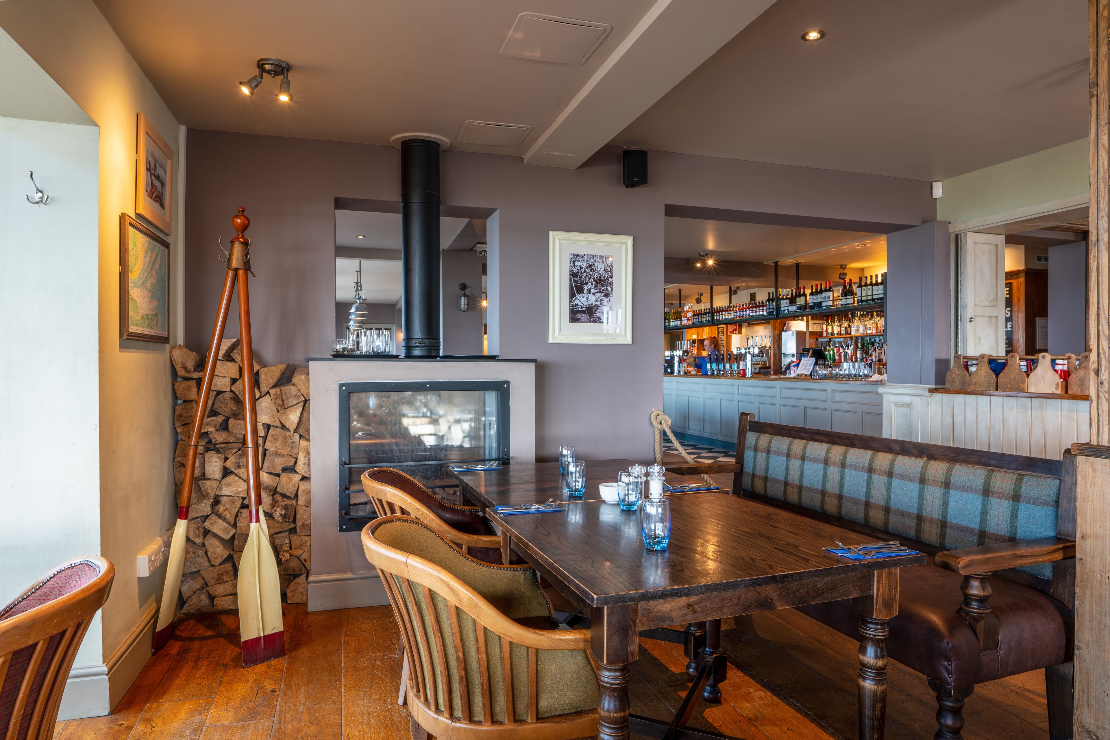A dining area with a wooden table, cushioned chairs, a bench, and a bar in the background.