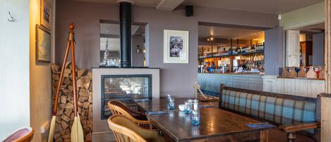 A dining area with a wooden table, cushioned chairs, a bench, and a bar in the background.