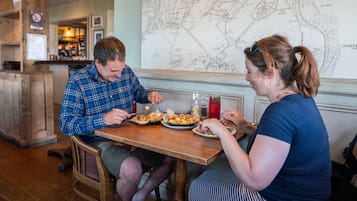 A wooden table with two people dining, a map on the wall, and a bar in the background.