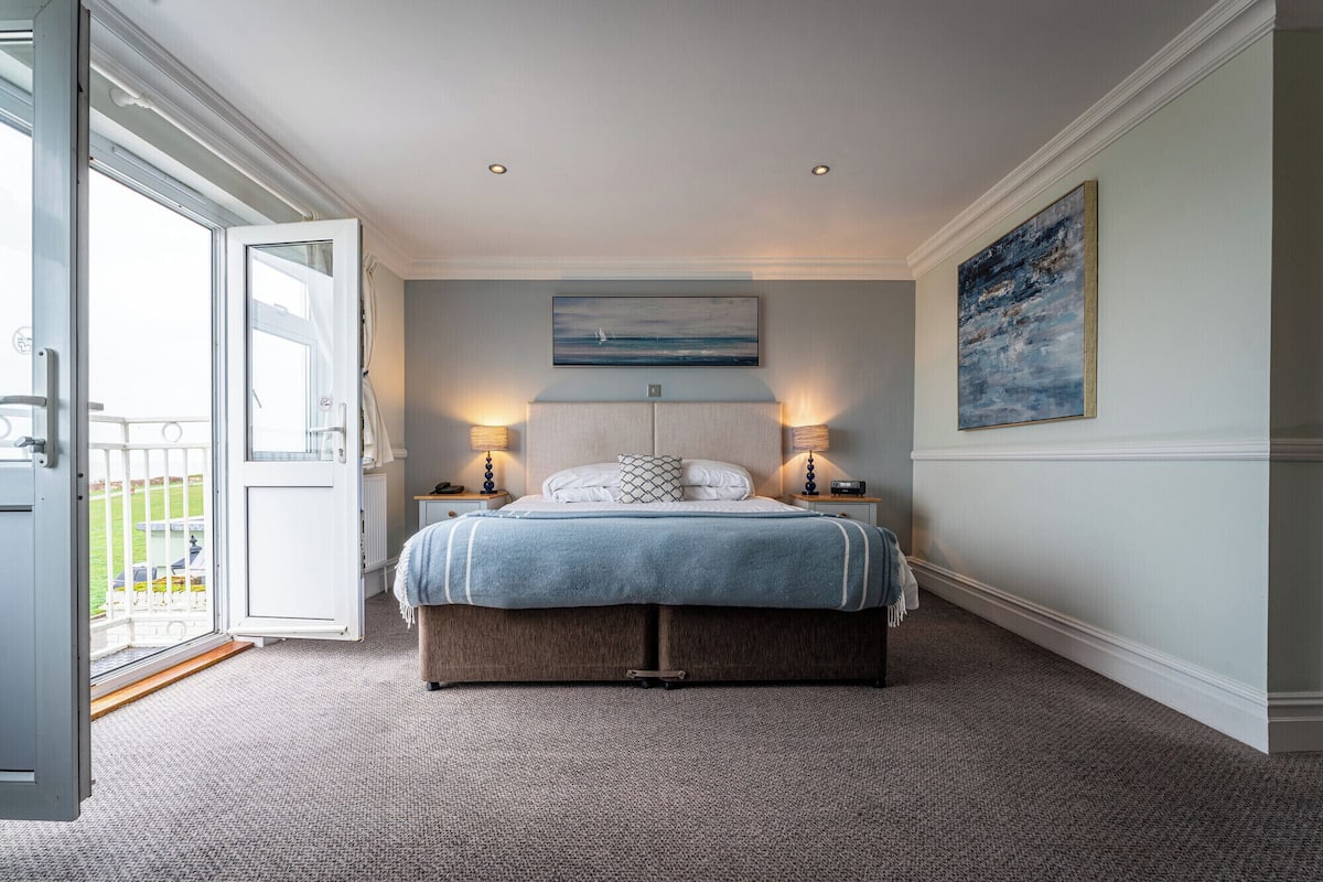 A bedroom with a bed, two bedside lamps, a painting, and a view through an open door.