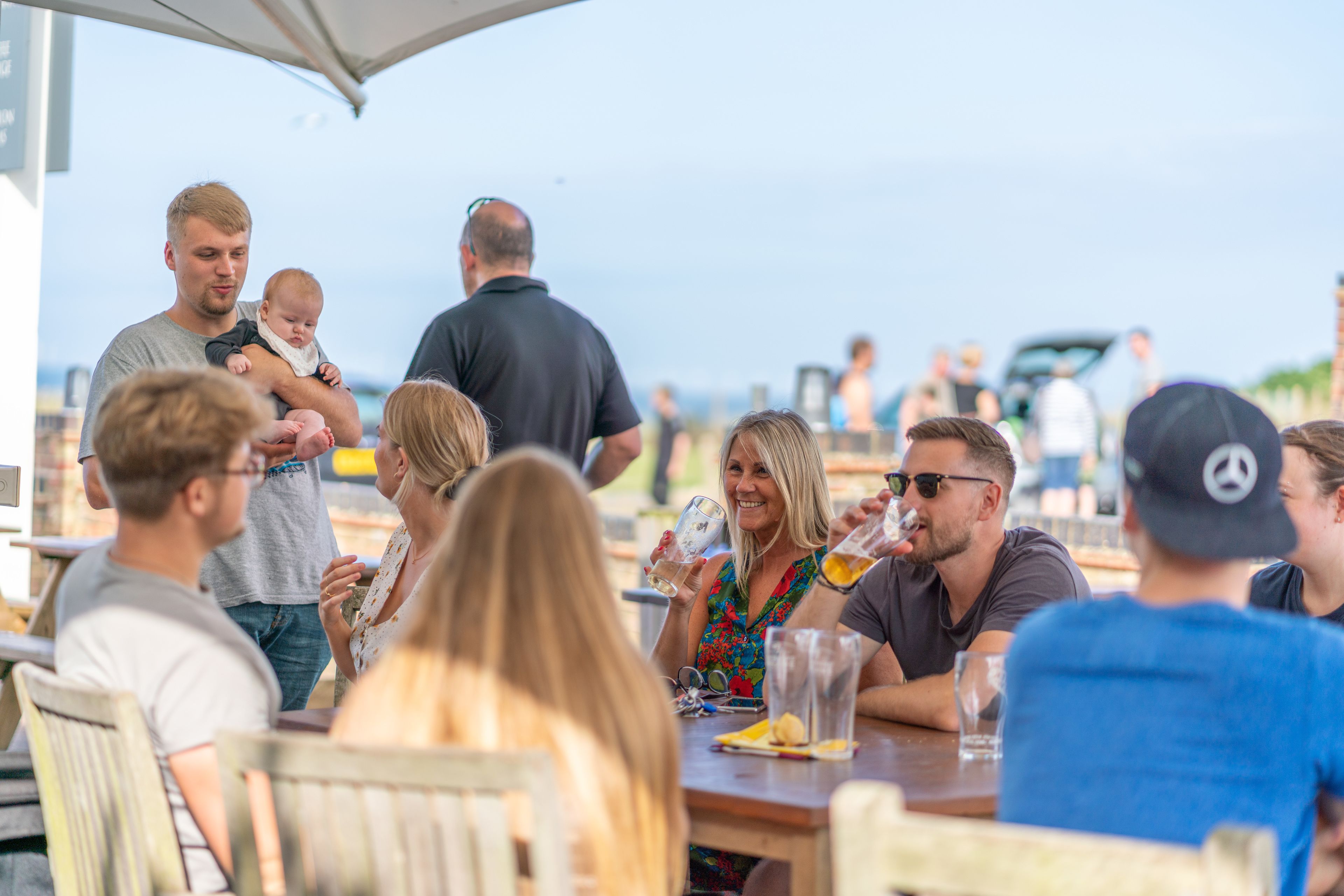 A group of people sitting at an outdoor table, some holding drinks.