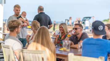 A group of people sitting at an outdoor table, some holding drinks.
