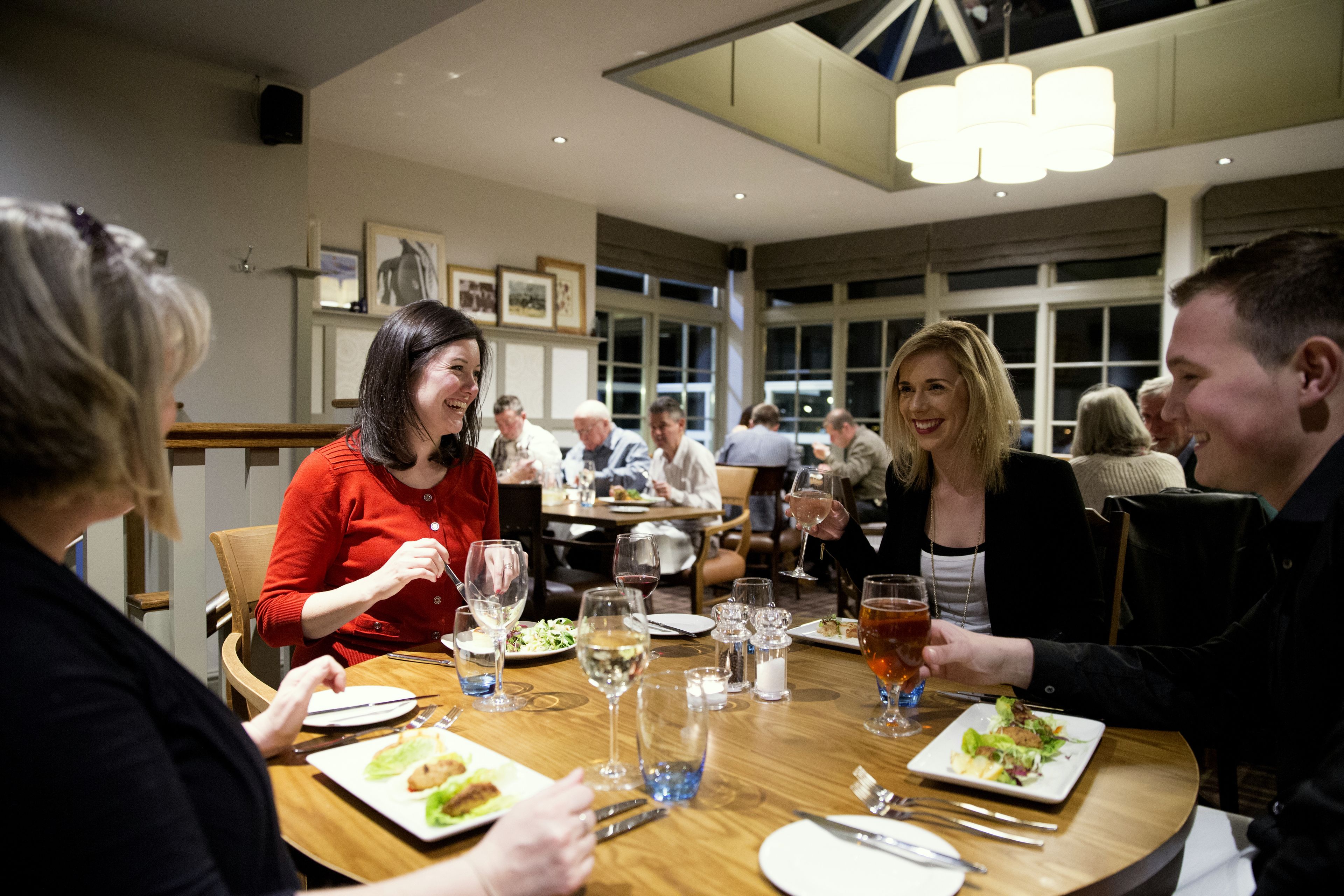 A group of people dining at a restaurant with wooden tables and chairs.
