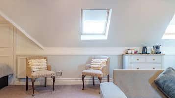 A room with a high ceiling, a skylight, a white dresser, two patterned chairs, a grey sofa, and a carpeted floor.