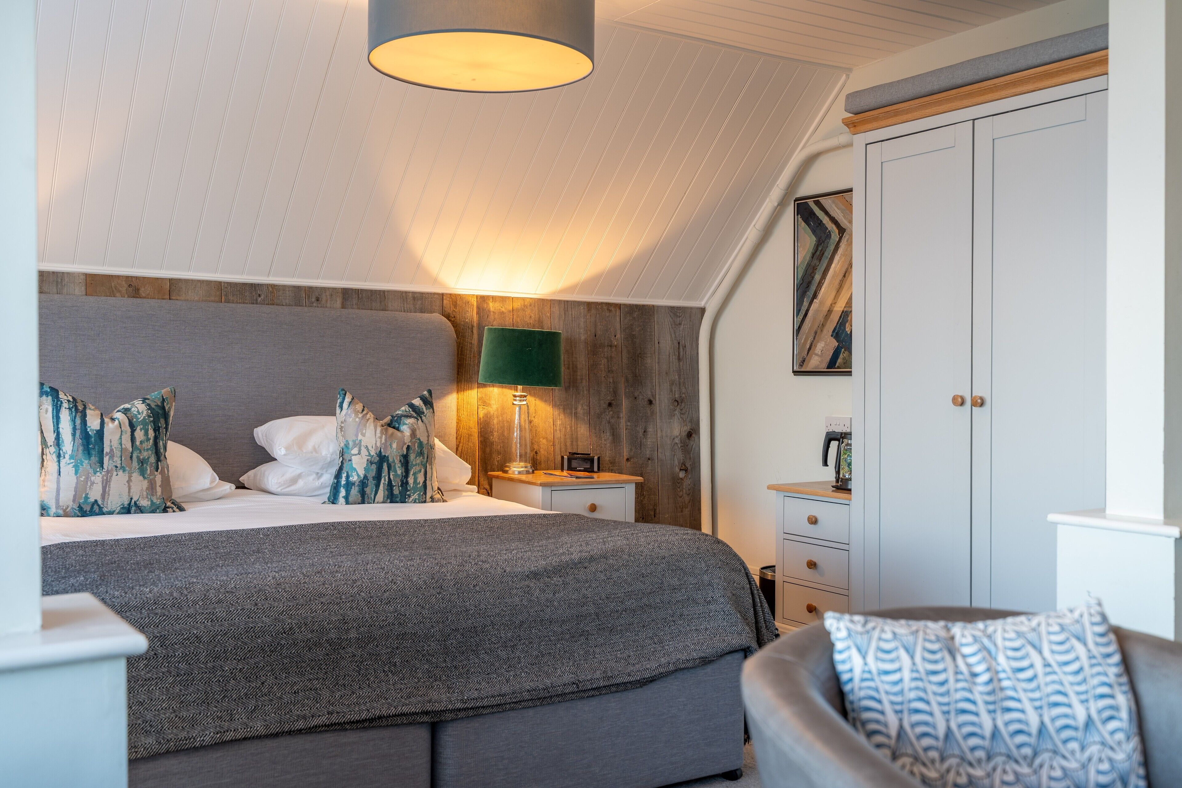 Et soveværelse med en stor seng, et natbord med lampe, et klædeskab og en stol.