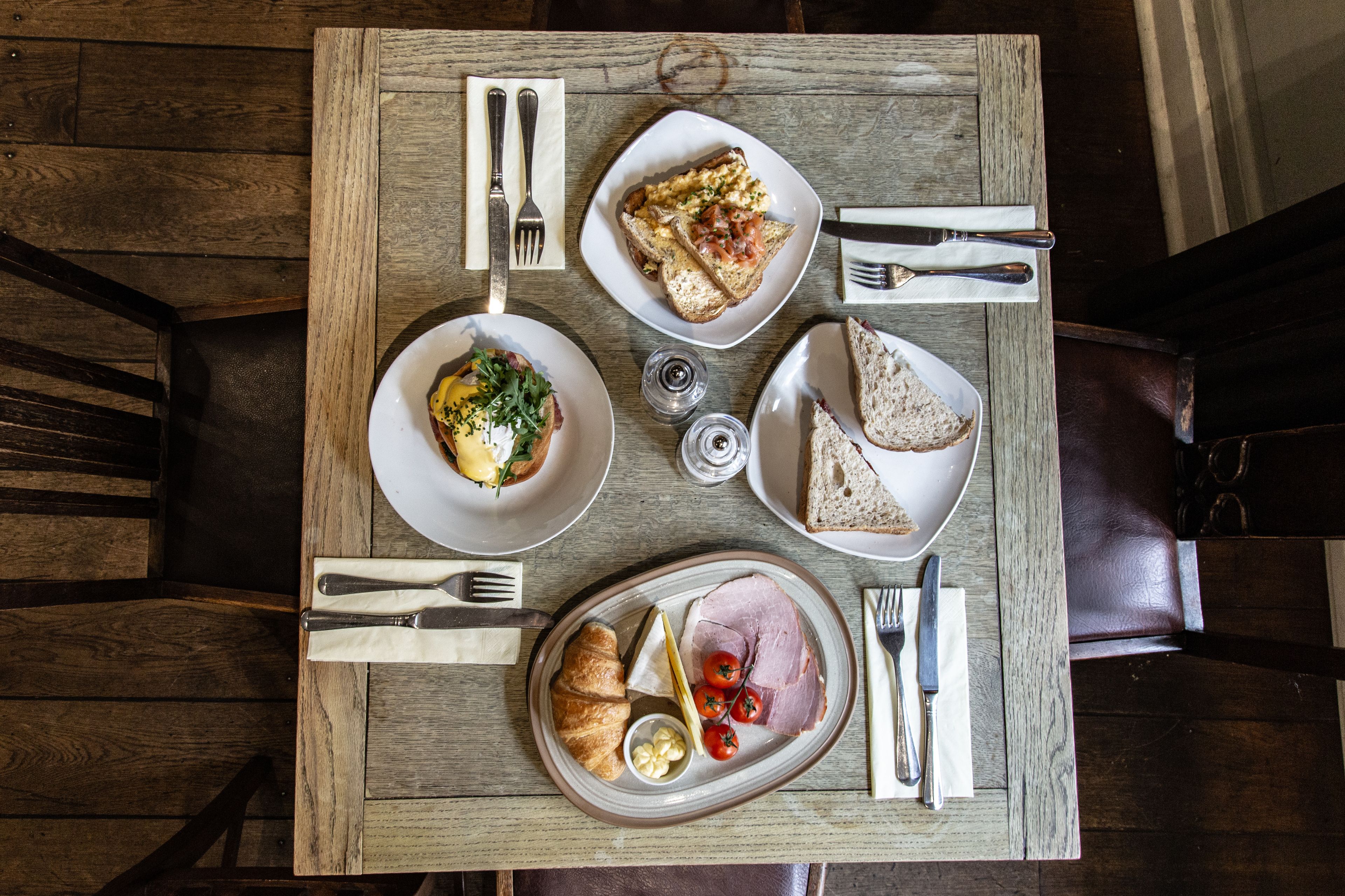 A wooden table with breakfast items including eggs, toast, ham, and croissants.