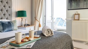 Habitación de hotel con cama, mesita de noche con lámpara, ventana con cortinas y vista al exterior.