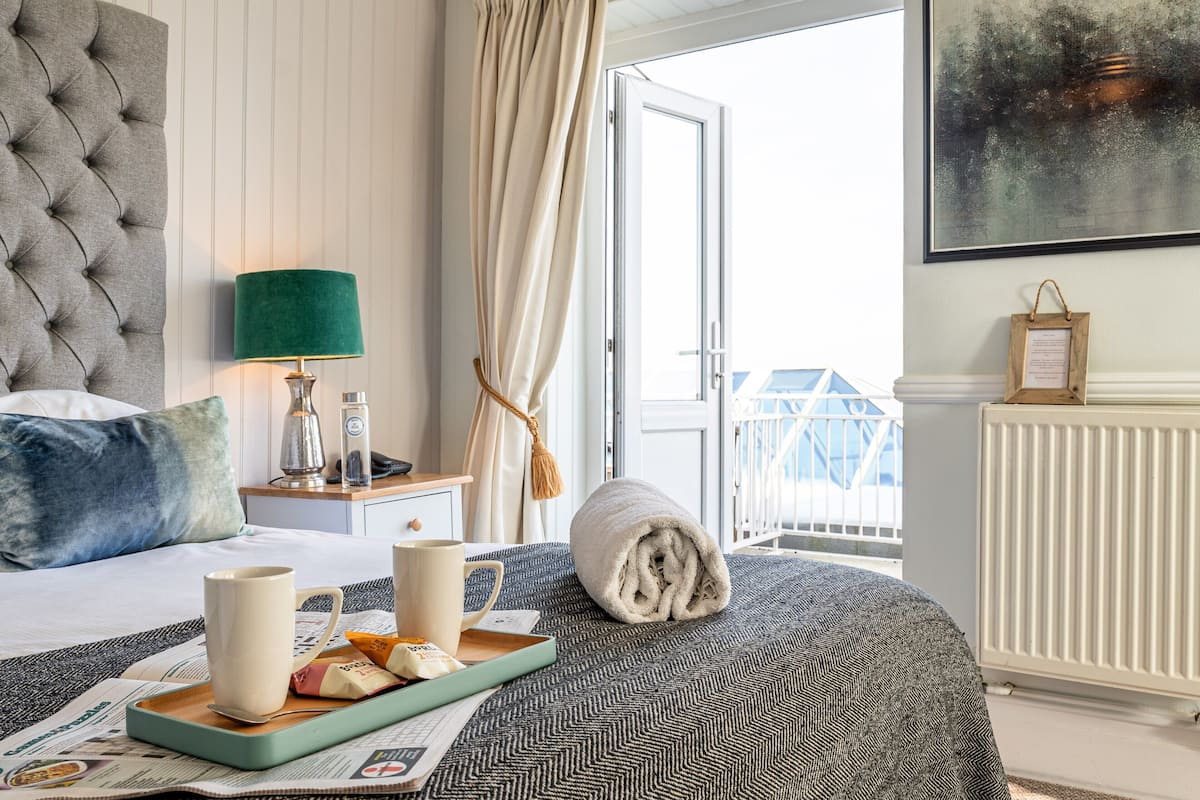 A hotel room with a bed, a bedside table with a lamp, a window with curtains, and a view of the outside.