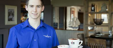 A person in a blue shirt holding a tray with a cup of coffee and a small bowl.