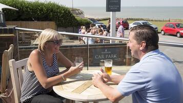 Two people seated at a table with a view of the sea and a sign indicating 'The Botany Bay'.