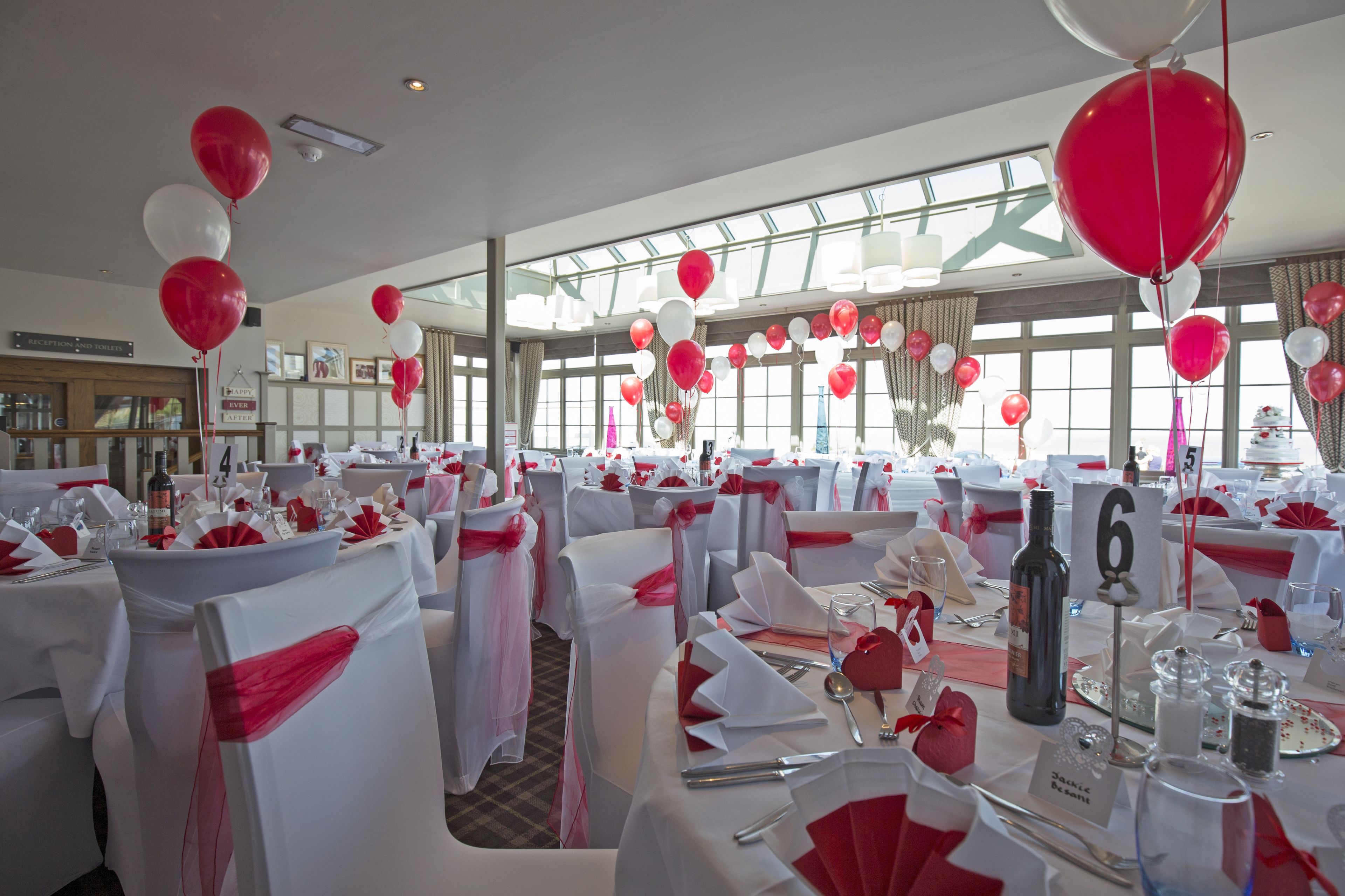 A banquet hall with round tables set for a formal event, adorned with red and white decorations.